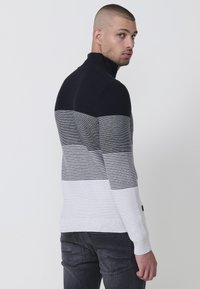 Gestreifter Pullover mit hohem Kragen, der von Marineblau über Grau bis Weiß verläuft. Weicher Strickstoff mit horizontalen und vertikalen Streifen.