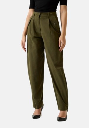 Donna che indossa pantaloni a gamba larga a vita alta verde oliva con pieghe frontali e tasche laterali con bottoni, abbinati a top nero e tacchi neri.