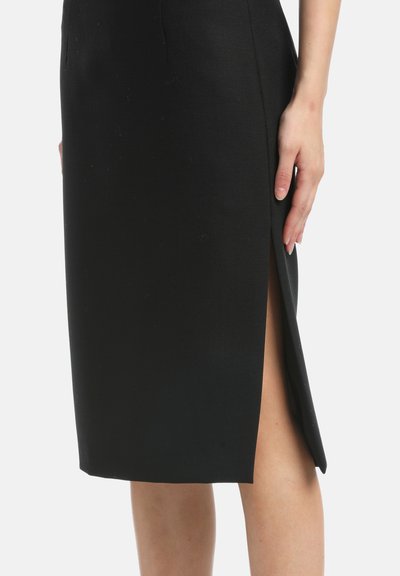 Hame rinta musta, jossa on tiukka muotoilu, sileä kankaan rakenne, polven pituinen leikkaus ja sivuhaalari lisäyksinä.