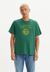 Grønn bomull t-skjorte med en gul Levi's-logo og sirkulært grafisk design. Løs passform med korte ermer og rund hals.