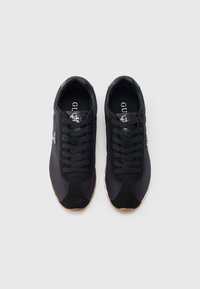 Μαύρα αθλητικά παπούτσια κατασκευασμένα από ύφασμα και σουέντ, με στρογγυλή μύτη, κλείσιμο με κορδόνια στο μπροστινό μέρος και λαστιχένια σόλα. Το λογότυπο εμφανίζεται στη γλώσσα.