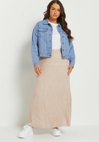 Jasnoniebieska dżinsowa kurtka na białym t-shircie, zestawiona z beżową, prążkowaną maksi spódnicą i białymi trampkami. Prosty design z casualowym wyglądem.