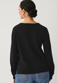 Maglione nero con maniche lunghe, scollo rotondo e orlo a coste. Il tessuto sembra morbido e liscio, con uno stile dal fit rilassato.