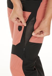 Roze en zwarte buitenbroeken met een mesh pocket en ritssluiting. Kenmerkt accentpanelen en duurzame stof.