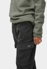 Olijfgroene sweatshirt met geribde manchetten, gecombineerd met zwarte cargobroek met een patchzak en een gestructureerde stof.