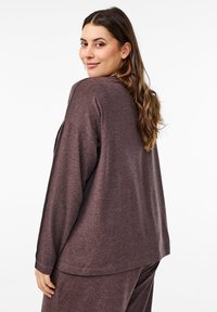 Haut à manches longues en mauve foncé, fabriqué en tissu doux. Il présente une coupe décontractée et un ourlet arrondi, avec un détail de couture visible sur les manches.