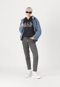 Jachetă pufoasă bleu deschis peste un hanorac negru GAP, blugi skinny gri și adidași albi. Modelul poartă ochelari de soare negri și cercei cerc.