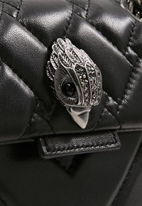 Svart quiltad läderhandväska med en silverfärgad metalldetalj i form av en fågel med detaljer och ett svart ädelstensöga.