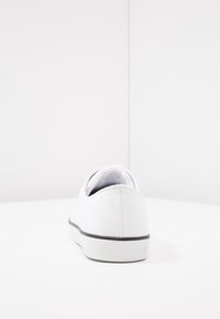 Weißer Canvas-Slipper mit strukturierter Oberfläche, Gummisohle und kontrastierenden grauen Akzenten. Verfügt über ein auf der Ferse eingeprägtes Logo.