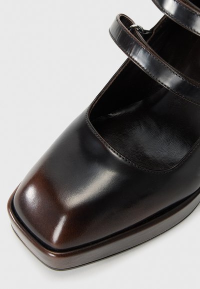 Chaussure Mary Jane en cuir noir avec un bout carré, deux sangles réglables et une finition lisse avec un léger talon.
