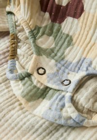 Monivärinen puuvillakangas, jossa on kuusikulmaisia kuvioita vihreänä, sinisenä, beigenä ja viininpunaisena, teksturoituna, rypytettynä yksityiskohtana ja metallisia neppareita.