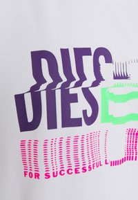 Förvrängd lila och rosa text "DIESEL" med gröna och rosa glitch-effekter på en vit tygbakgrund.