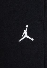 Černá látka s bílým vyšívaným logem Jumpman, zobrazujícím postavu ve vzduchu držící basketbalový míč. Hladká textura, minimalistický design.