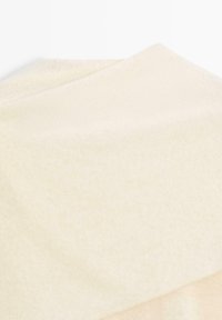 Blødt beige uldstof foldet med synlig struktur og subtile farvevariationer mod en hvid baggrund.