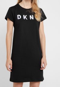 Černé bavlněné šaty s krátkými rukávy, na přední straně se nachází bílé vyšívané logo "DKN", jednoduchý design a volný střih.