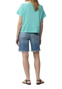 Licht aqua kortstondig T-shirt met een relaxte pasvorm, gecombineerd met omgeslagen blauwe denim shorts. Platte sandalen maken de outfit compleet.
