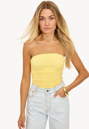 Haut jaune sans bretelles avec un motif en dentelle texturée, associé à un jean taille haute bleu clair. Bracelet doré notable au poignet.