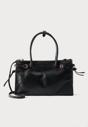 Sac à main en cuir noir avec deux poignées supérieures, des sangles latérales réglables avec boucles, et une bandoulière amovible sur fond blanc.