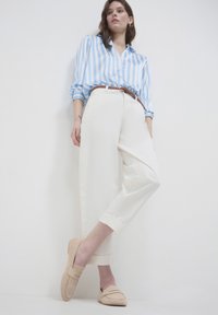 Helles blau-weiß gestreiftes Blusenshirt, cremefarbene weit geschnittene Hosen mit umgeschlagenen Säumen und beigen Loafers mit dezentem Stickdetail.