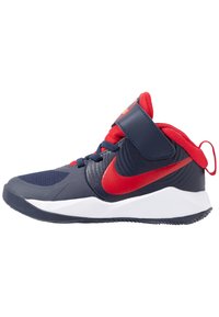 Navy ja punaset urheilukengät, joissa on teksturoitu synteettinen päällinen, nauhatyyppinen muotoilu, säädettävä hihna ja valkoinen kumipohja. Logo on esillä sivussa.