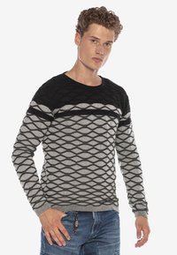 Schwarzer und grauer Langarmpullover mit strukturiertem Rautenmuster, rundem Ausschnitt und gerippten Bündchen. Kombiniert mit blauen Jeans.