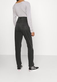 Vaqueros grises de cintura alta con una textura suave y bolsillos traseros, combinados con una camiseta de manga larga gris clara y zapatillas negras.
