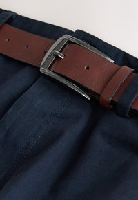 Ceinture en cuir marron avec une boucle argentée attachée autour d'un pantalon en tissu bleu foncé.