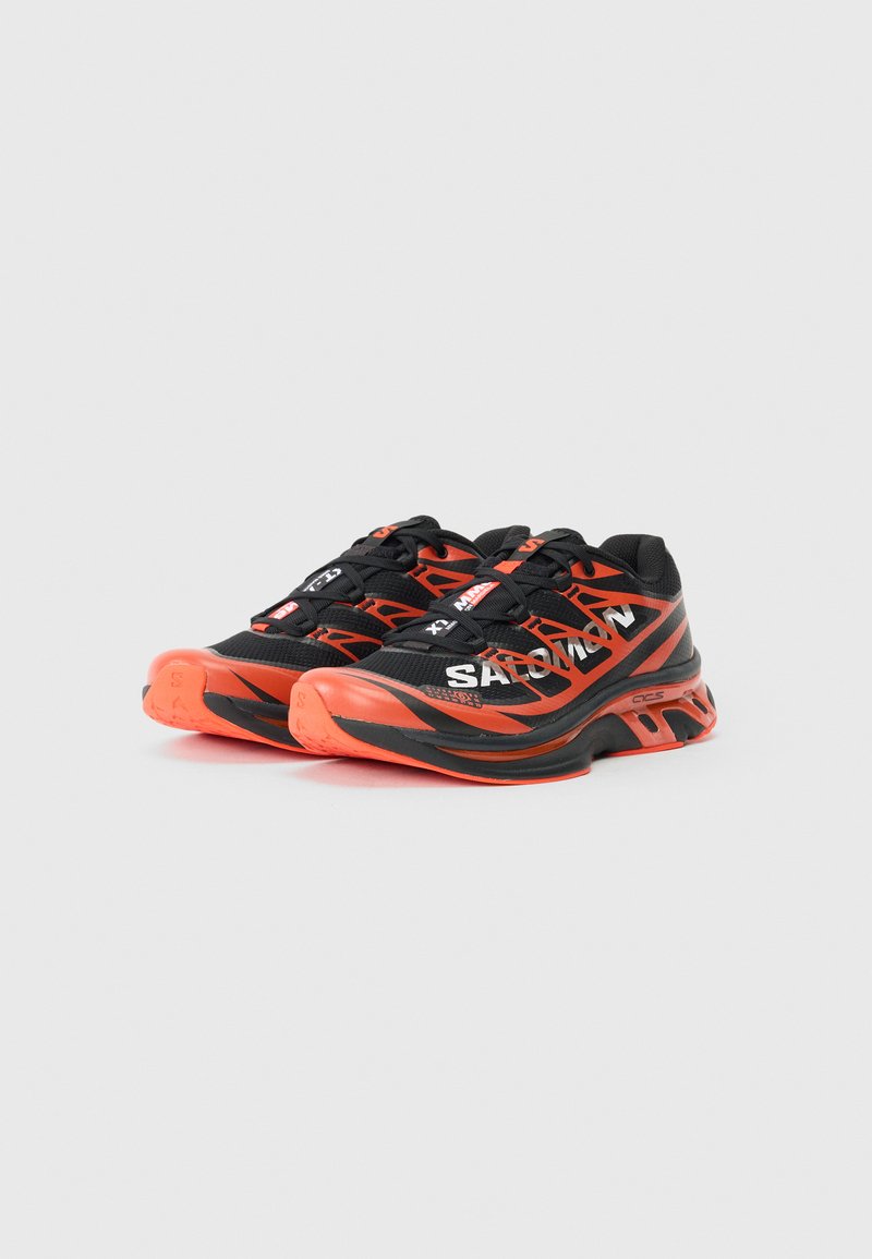 Baskets de sport noires et orange avec une tige en mesh, semelle rembourrée et talon renforcé. Présente des lacets et des accents de logo sur le côté.