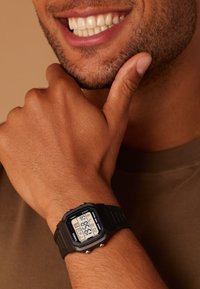 Montre numérique avec un bracelet en silicone noir, cadran rectangulaire affichant l'heure, la date et d'autres fonctions en blanc et bleu.
