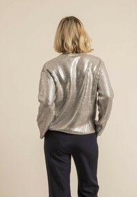 Veste ribbed métallique argentée avec une coupe ample. Dotée d'un col plat, de manches longues et d'une texture lisse. Associée à un pantalon sombre.