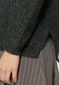 Ciemnoszara sweter z dzianiny o ryflowanej fakturze, z bocznym rozcięciem i małą czarną metką na dolnym brzegu, w połączeniu z spódnicą w prążki.