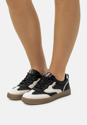 Zapatillas negras y blancas con una superficie texturizada, con cordones, suela de goma y acentos de color contrastante.