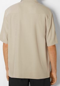Short-sleeve beige shirt made of smooth fabric, featuring a collared neckline and a relaxed fit with a plain back design.