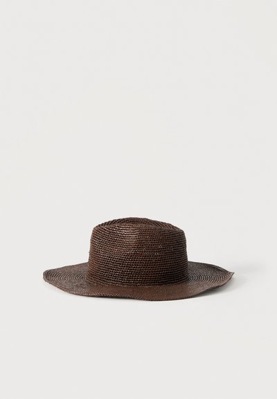 Chapeau marron tissé à large bord avec une calotte arrondie, posé à plat sur un fond clair uni.
