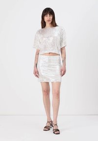 Top corto bianco in paillettes abbinato a una mini gonna in paillettes coordinata. L'outfit presenta una vestibilità ampia e maniche corte, con una texture liscia.