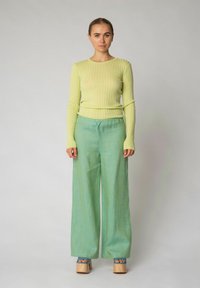 Maglietta verde a righe con maniche lunghe, abbinata a pantaloni larghi verde chiaro. Il modello indossa scarpe con plateau in legno con cinturini blu.