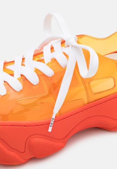 Διαφανές πορτοκαλί αθλητικό παπούτσι με λευκά κορδόνια, χοντρή κόκκινη σόλα και μοτίβα στην επάνω επιφάνεια. Σημειώστε το στρογγυλεμένο σχήμα της φτέρνας.