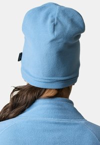 Beanie in pile azzurro con una texture morbida e un risvolto piegato, caratterizzato da un piccolo tag con logo sul lato. Indossato con un top coordinato in pile.