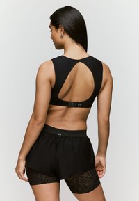 Bralette negro con un diseño de espalda con corte y cierre ajustable. Combinado con pantalones cortos negros con detalles de encaje y una cinturilla texturizada.