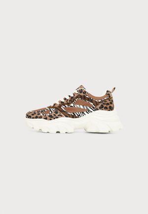 Chunky sneaker με πάνελ λεοπάρ και ζέβρας, λευκά κορδόνια και παχύ λευκό πέλμα σε ουδέτερο φόντο.