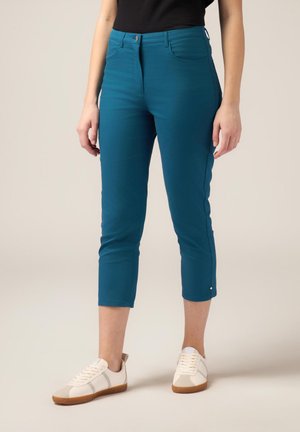 Pantalones cortos en color aguamarina con una textura suave, bolsillos frontales y cierre de botón. Combinados con zapatillas blancas con acentos en color marrón.