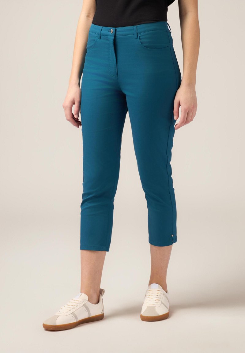Pantaloni cropped turchesi con una texture liscia, tasche anteriori e chiusura con bottone. Abbinati a sneaker bianche con dettagli color pelle.