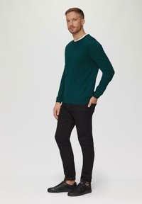 Grüner Pullover mit rundem Halsausschnitt, aus weichem Material gefertigt. Kombiniert mit schmal geschnittenen schwarzen Hosen und schwarzen Sneakers.