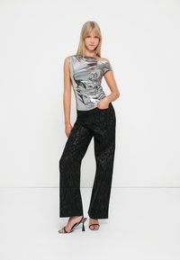 Top argentato a spalla unica con una finitura lucida, abbinato a pantaloni neri a gamba larga con una sottile stampa animale e décolleté in bianco e nero.
