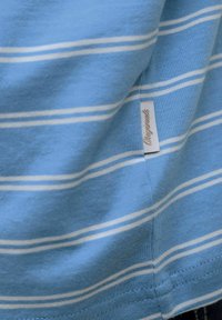 Hele sinine kangas, millel on valged horisontaalsed triibud ja väike valge silt õmmeldud küljeseemnele.