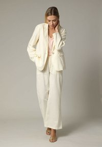 Linnenmix pak in off-white met een op maat gemaakte blazer met een enkele knoop en wijde broekspijpen, gecombineerd met een lichtroze top.