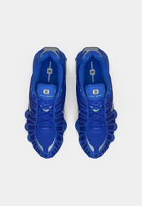 Baskets Nike Shox bleues avec un dessus en maille, une semelle en caoutchouc et des accents argentés. Elles présentent un design structuré avec plusieurs pods de rembourrage.