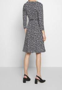 Czarna sukienka z białym nadrukiem liści, trzyczwarte rękawy, dopasowany talia, rozkloszowana spódnica i buty na słupku o fakturowanej podeszwie.