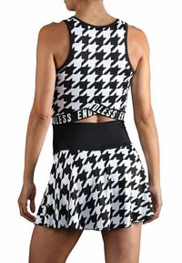 Mujer vestida con un top sin mangas de corte corto con un patrón de jaquard en blanco y negro y una falda a juego que lleva el texto "ENDLESS" en la cinturilla, de pie con la espalda visible.