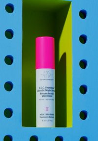T.L.C. Framboos glycolic night serum in a white tube with a pink cap, displayed within a bright blue and green geometric frame.